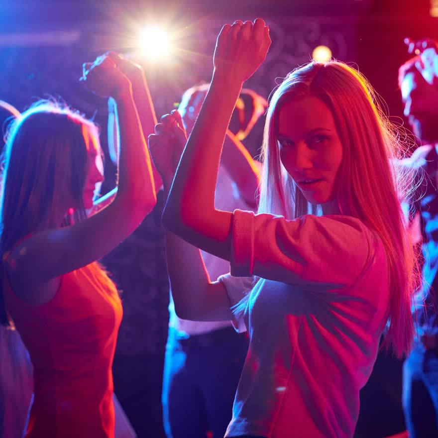 Grupo bailando y brindando en un club con luces de noche